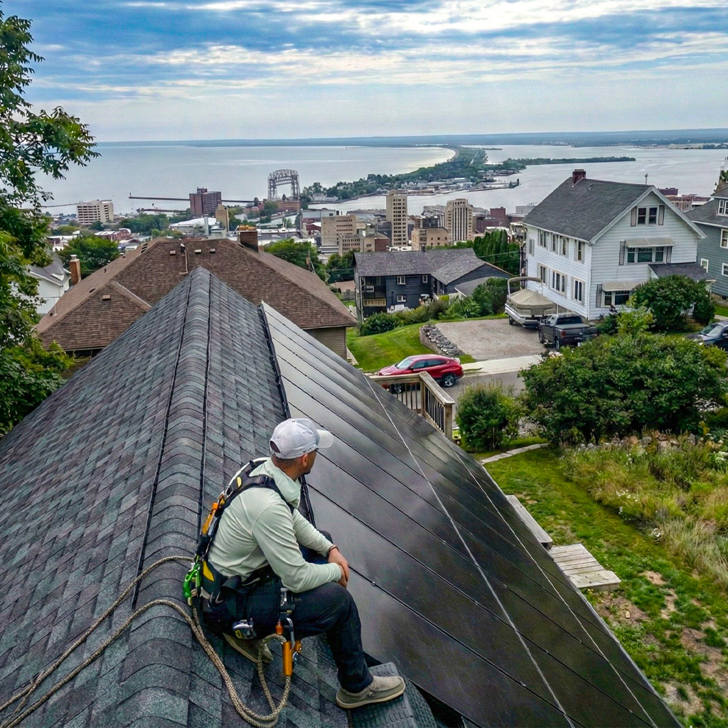 Benson Electrical Company employee on roof with solar panels looking over Duluth, MN, lift bridge, and to Superior, WI